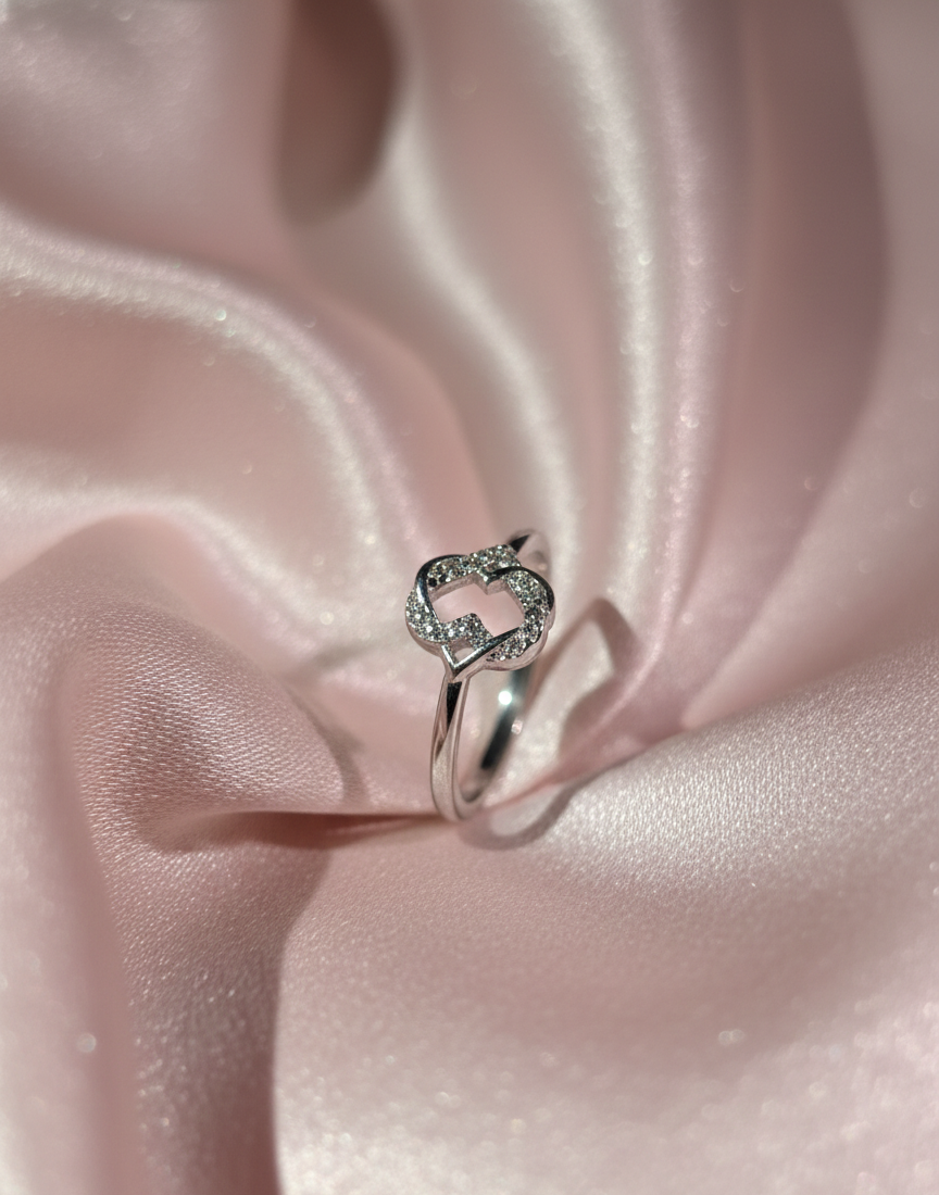 Silver ring with a heart design on pink satin fabric